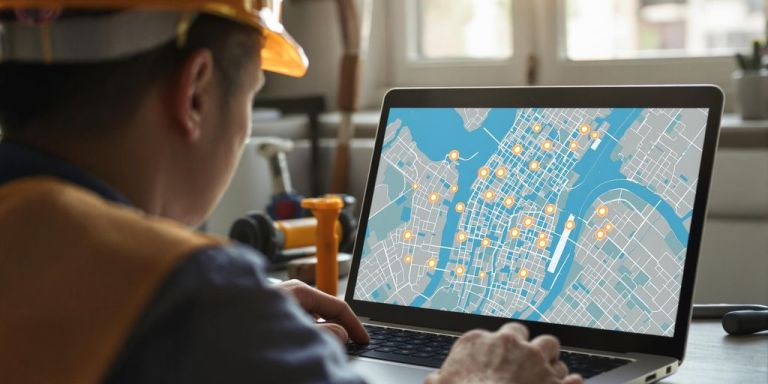 Contractor using laptop, city map on screen.