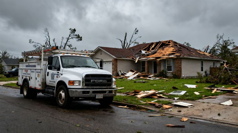Contractor truck near storm-damaged house.